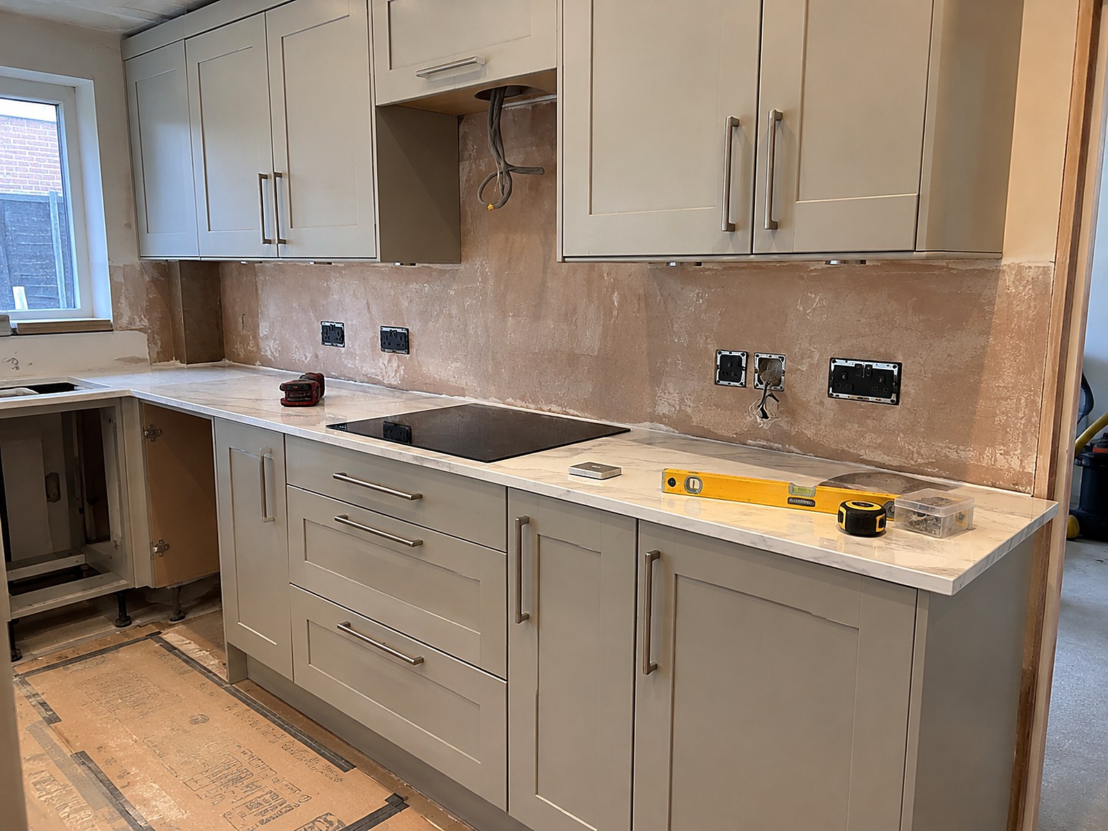 Kitchen installation in progress with greige shaker units and white worktops